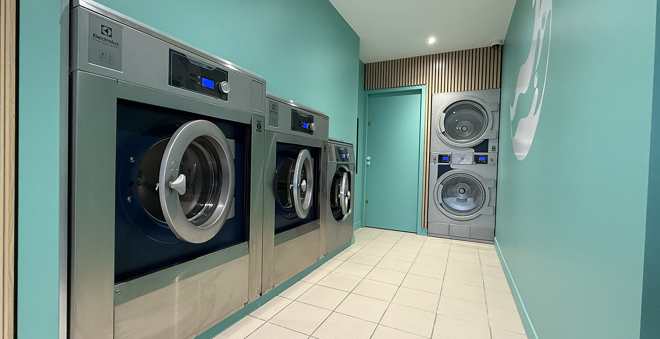 Espace intérieur de la Laverie de Retz : 3 lave-linge et séchoir double Electrolux sur murs vert sauge